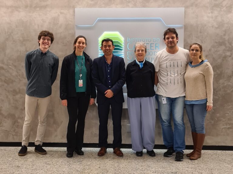 Grupo de seis pessoas, incluindo o palestrante Gabriel Sawakuchi, posa em frente a um painel com o logo do ICESP.