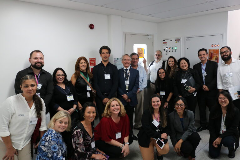 Grupo de 19 pessoas, composto por pesquisadores do LATAM Biorepository e convidados, posa em frente ao LATAM Biorepository.